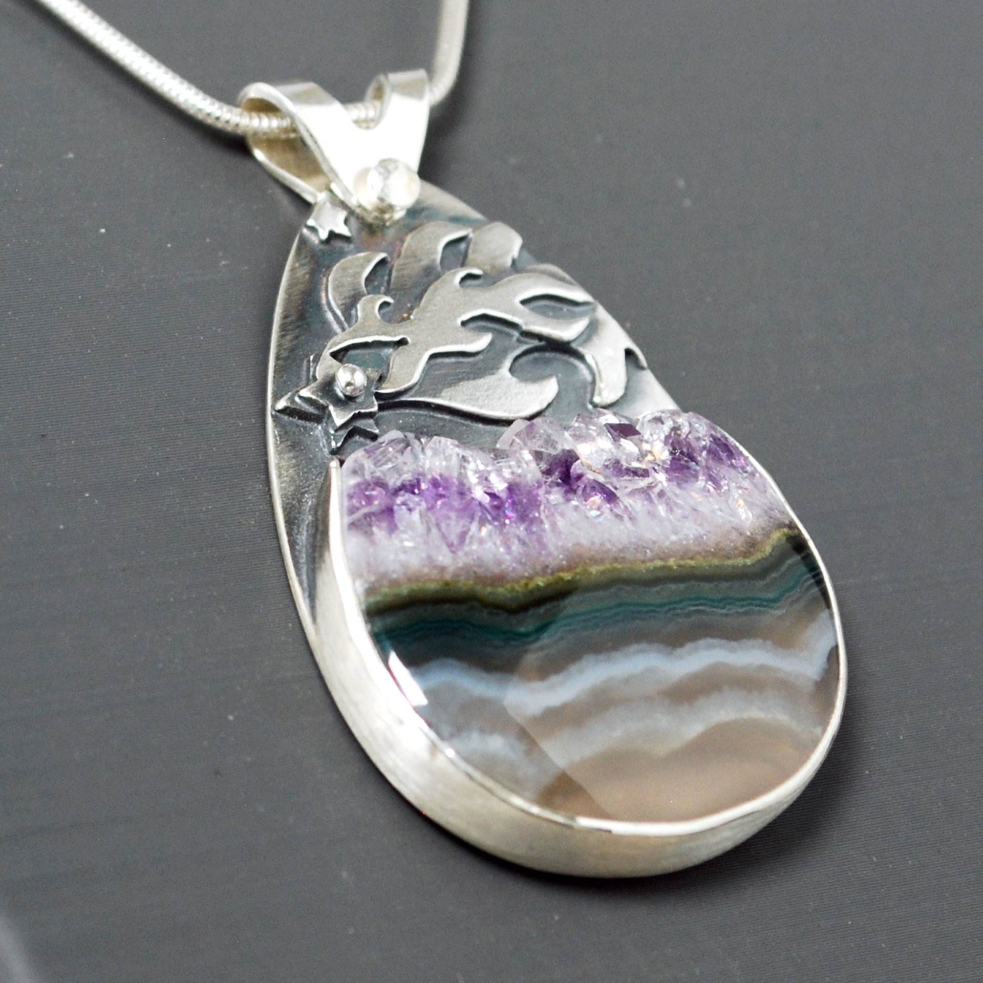 Silver pendant with Amethyst in Quartz cabochon, silver falling star above stone, close-up
